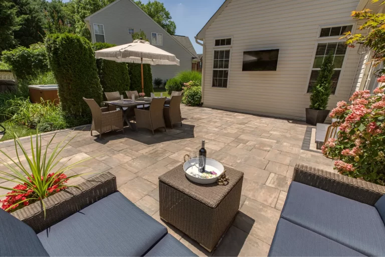 Spacious backyard patio with outdoor dining set, umbrella, wicker furniture, and garden plants.