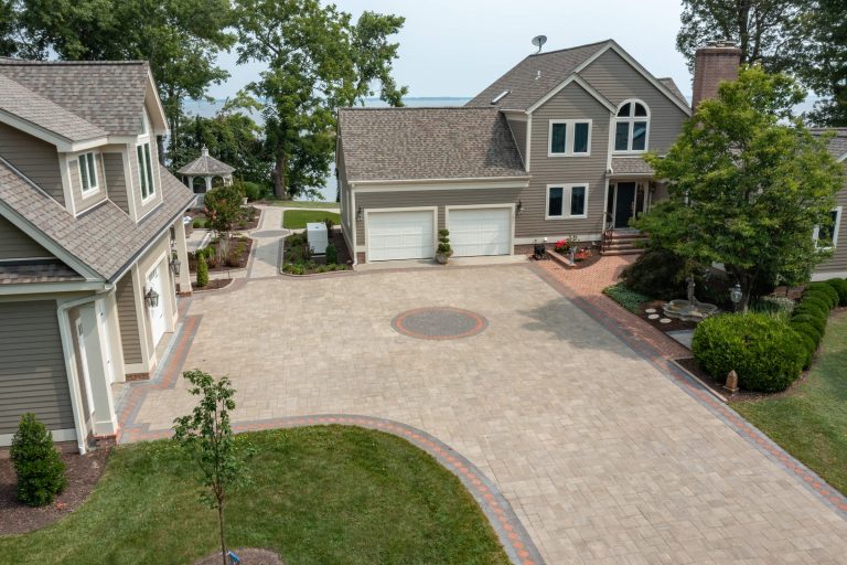 A large suburban home with a spacious paved driveway, two garages, and landscaped greenery.