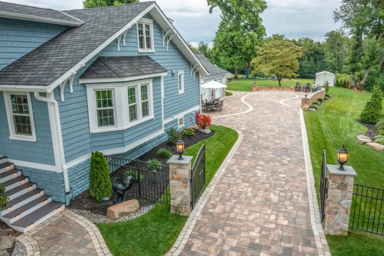 A paved driveway beside a blue house with a landscaped yard and outdoor seating area.