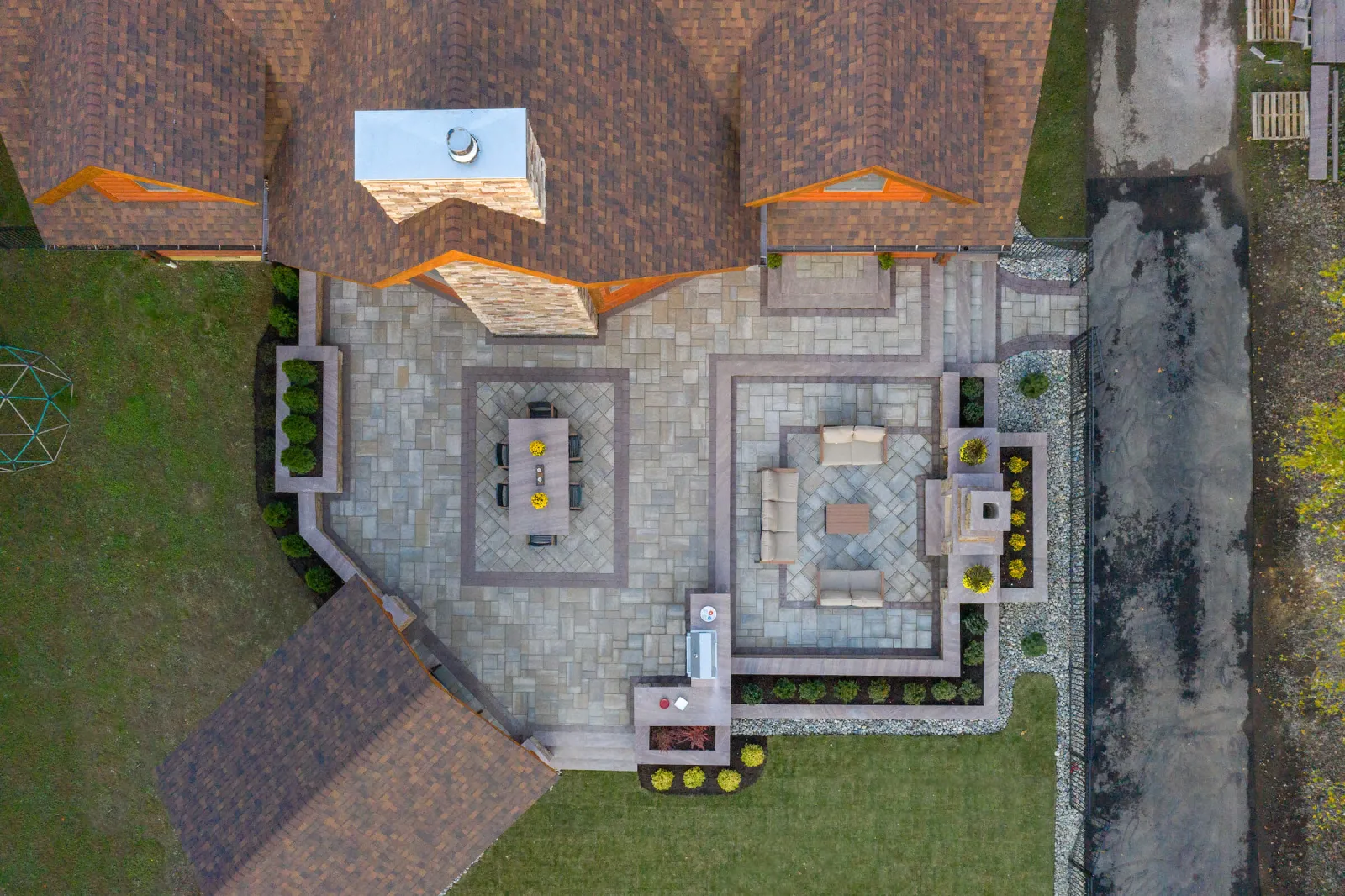 Aerial view of a large stone patio with seating areas, dining table, and landscaping around a house.