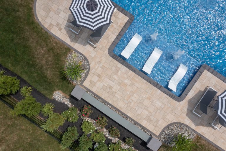 Aerial view of a pool with in-water loungers, umbrellas, patio, and landscaped garden.
