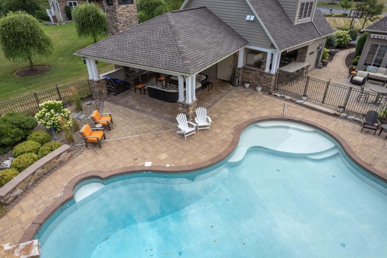 A backyard pool with patio seating, lounge chairs, and a covered outdoor kitchen area.