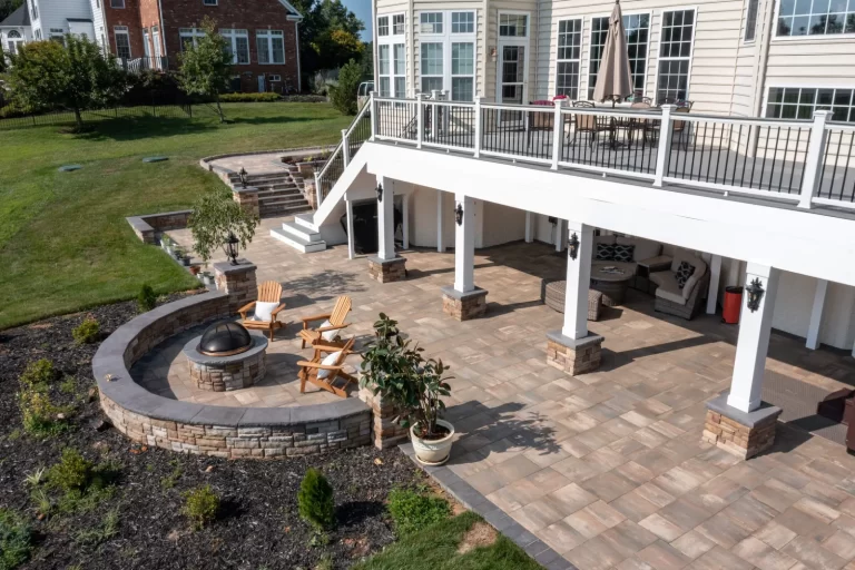 Spacious backyard patio with fire pit, chairs, covered seating area, and stairs leading to an upper deck.
