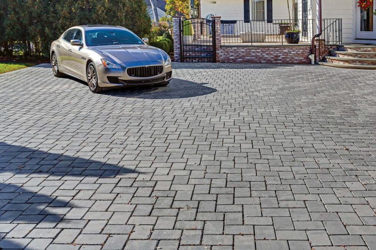 A silver car parked on a large, clean driveway made of rectangular gray pavers in front of a house.