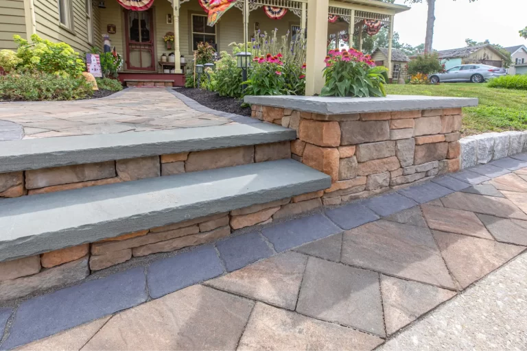 Stone steps and a short retaining wall lead to a porch with flowers and festive decorations in front of a house.
