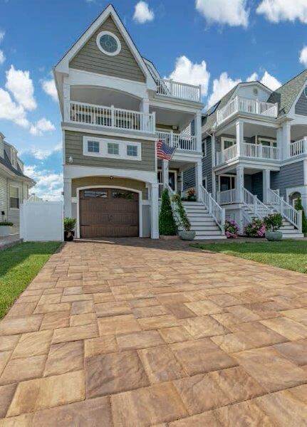 Three-story house with balconies, tan driveway, white railings, and American flag, under a blue sky.