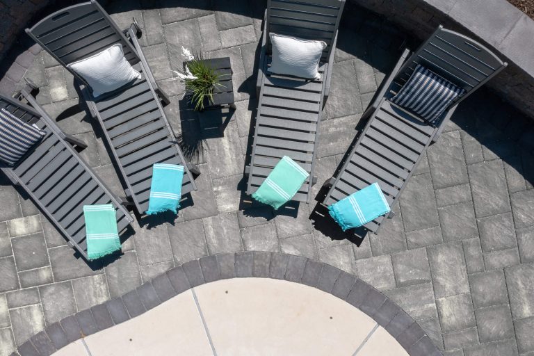 Five gray lounge chairs with pillows and turquoise towels arranged on a stone patio by a curved pool edge.