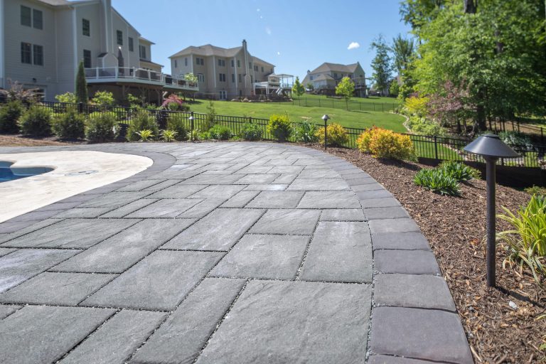 Gray stone patio with garden lights, mulch, and green landscaped yard in a suburban neighborhood.