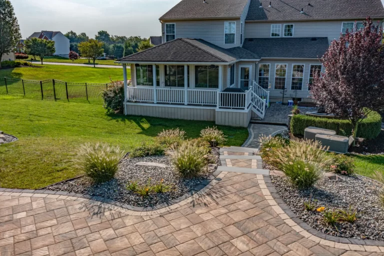 Backyard with a paved patio, landscaped garden, and a screened porch attached to a two-story house.