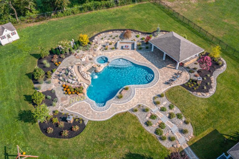 Aerial view of a backyard pool with a hot tub, patio, gazebo, and landscaped garden areas.