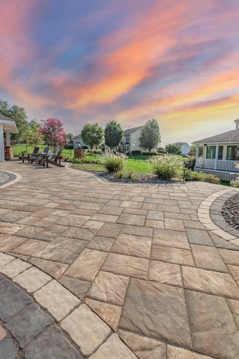 Spacious stone patio with chairs, garden landscaping, and a vibrant sunset sky in the background.