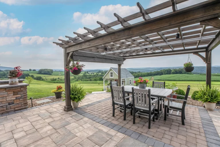 Outdoor patio with a pergola, dining table and chairs, overlooking green fields and distant hills.