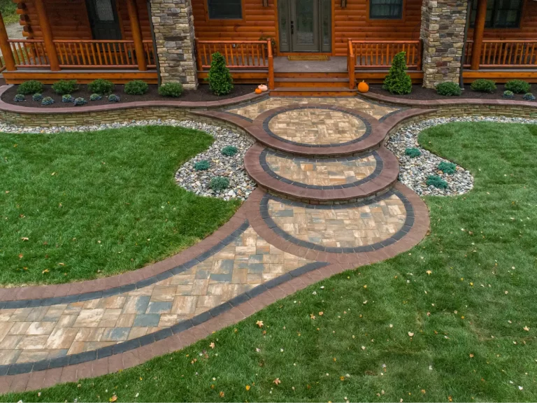 Circular stone steps with curved walkways and landscaping in front of a wooden house with a porch.