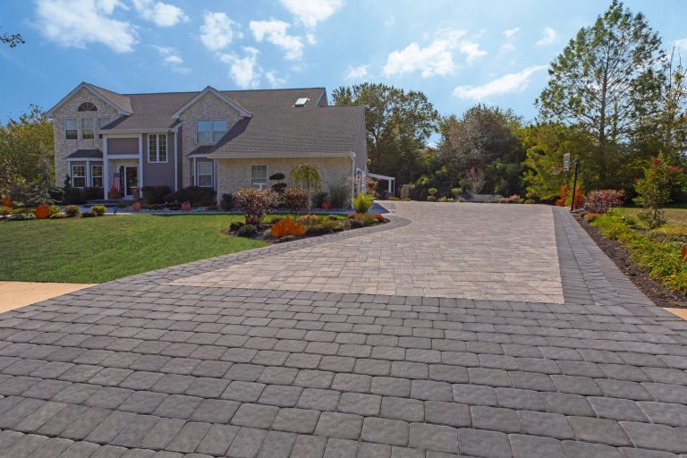 Large house with landscaped yard and a wide, patterned stone driveway on a sunny day.