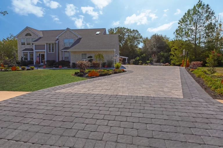 A large house with a wide, patterned stone driveway and well-maintained landscaping under a blue sky.