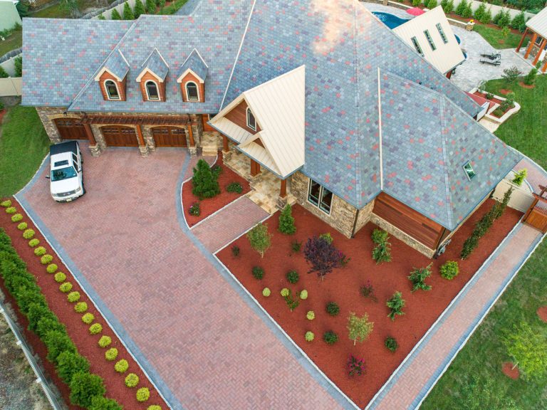 Aerial view of a large house with a driveway, parked white vehicle, and landscaped front yard.