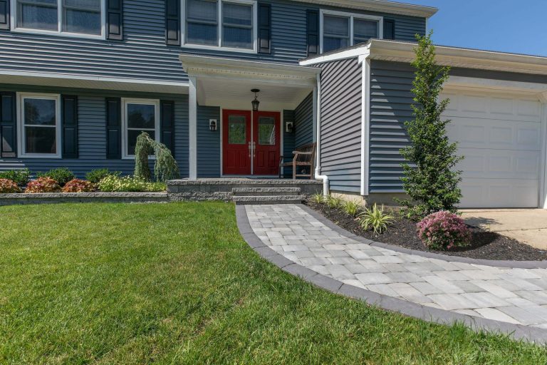 House exterior with red double doors, gray siding, garage, stone walkway, and landscaped front yard.