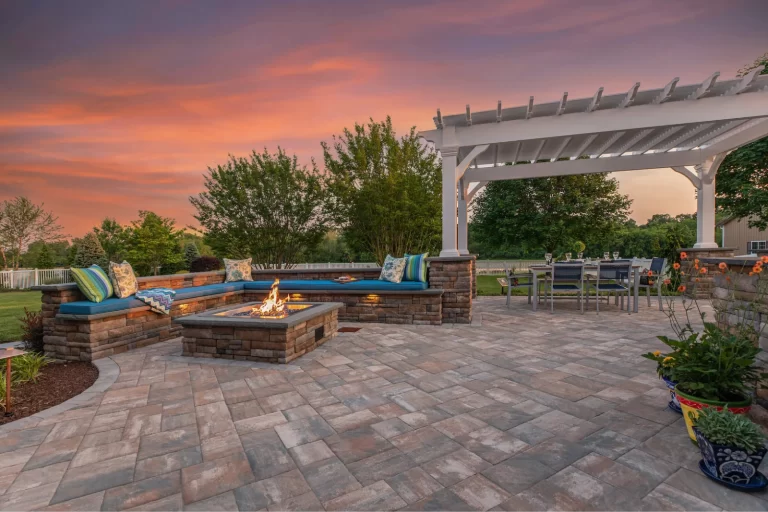 Spacious patio with fire pit, built-in seating, pergola, outdoor dining area, and sunset sky in the background.