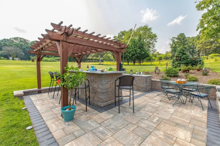 A patio with a pergola, bar seating, and outdoor table set in a grassy backyard garden.