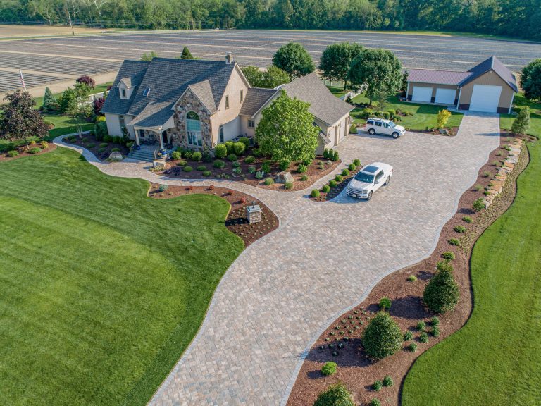 Aerial view of a house with a long, curving driveway, landscaped yard, and cars parked outside.