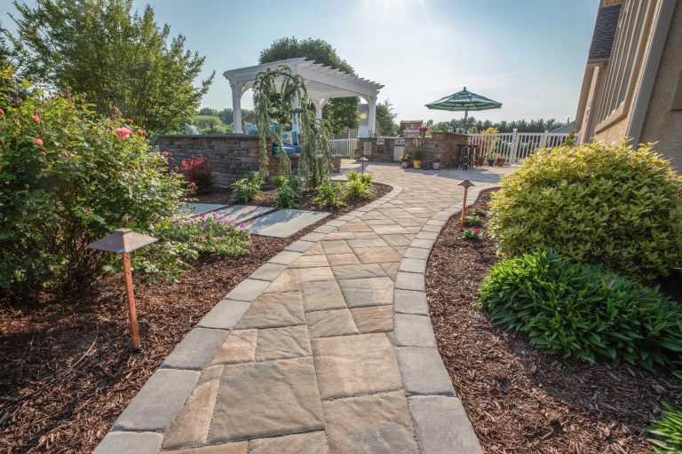 Curved stone walkway through landscaped garden, leading to patio with pergola and outdoor seating.