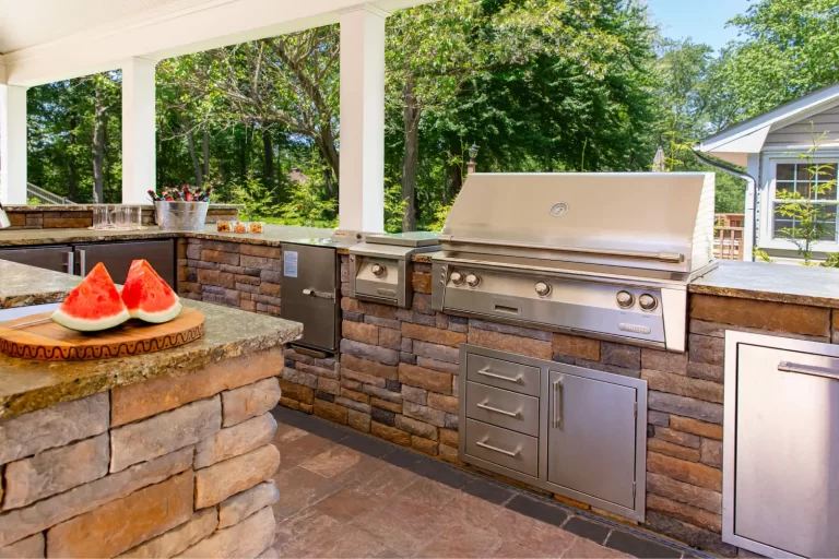 Outdoor kitchen with a built-in grill, stone countertops, and watermelon slices on a cutting board.