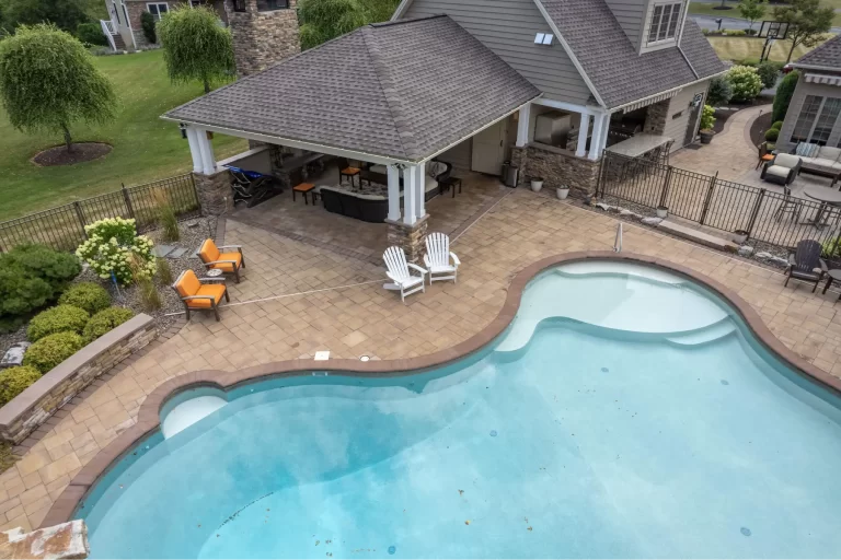 A backyard pool with lounge chairs, patio seating, and a covered outdoor kitchen area.