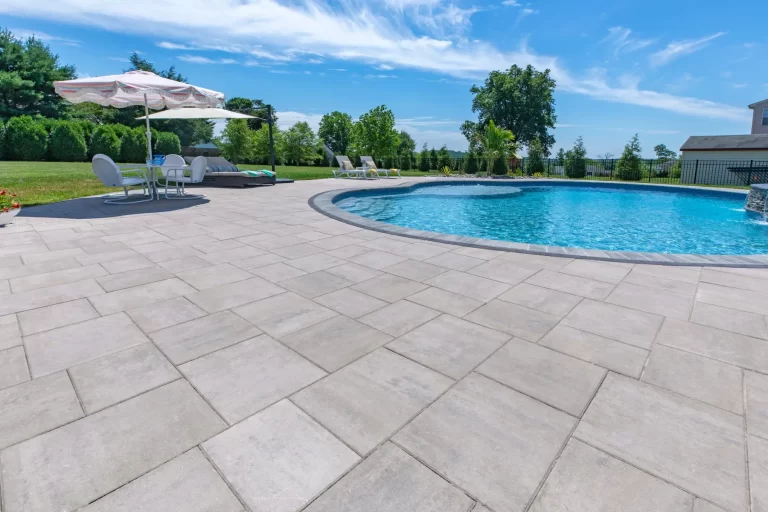 Sunny backyard with a swimming pool, lounge chairs, umbrellas, and trees in the background.
