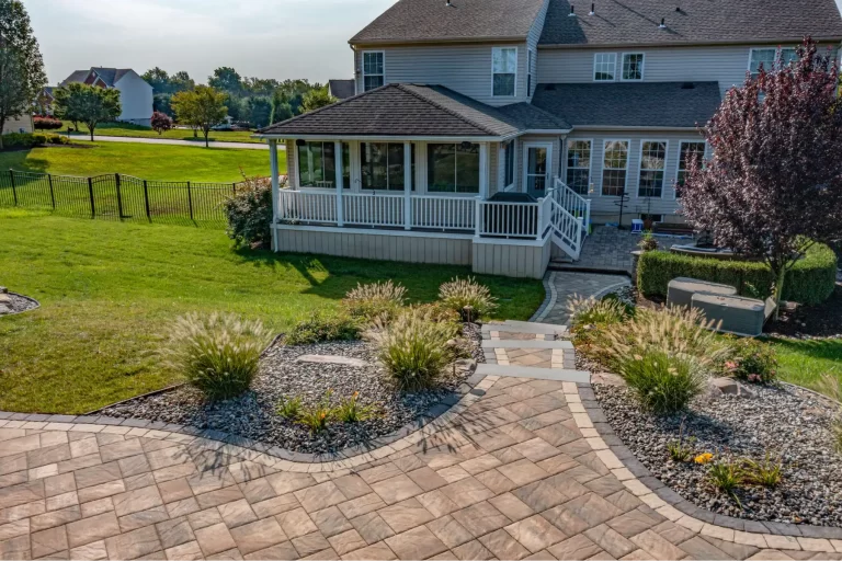 A backyard with a patio, landscaped garden, stone path, and a house with a screened porch.