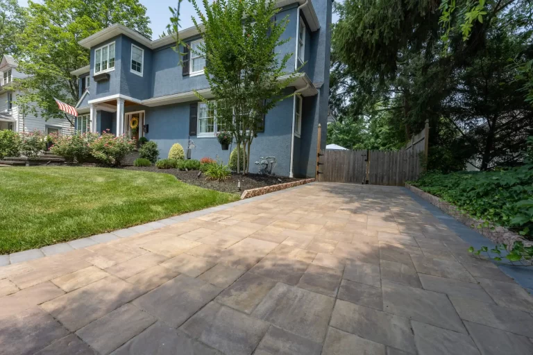 A blue two-story house with a paved driveway, green lawn, and trees in the yard.