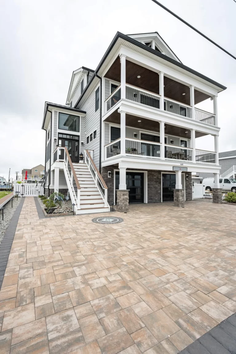 Three-story beach house with large balconies, wide steps, and a spacious stone-tiled driveway.