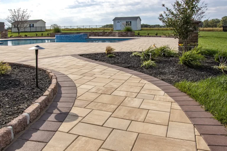 Curved stone walkway leads to a patio and pool, surrounded by landscaping and grassy lawn.