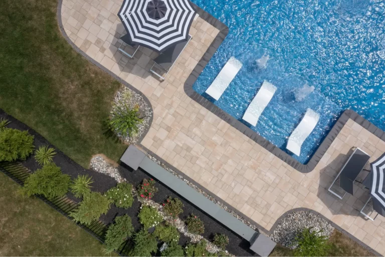 Aerial view of a pool with lounge chairs, patio umbrellas, and landscaped garden beside it.
