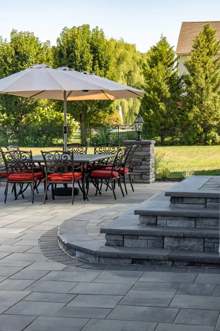 Patio with stone steps, table and chairs under a large umbrella, overlooking a grassy yard and trees.