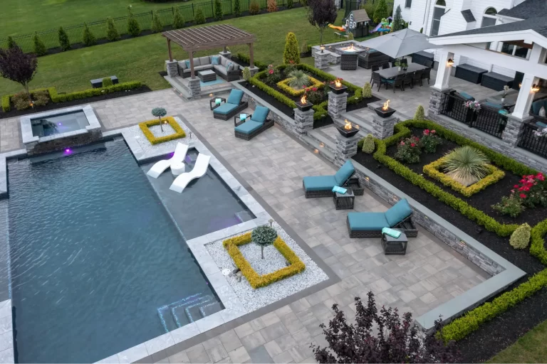 A modern backyard with a pool, lounge chairs, fire pits, pergola, and landscaped garden beds.