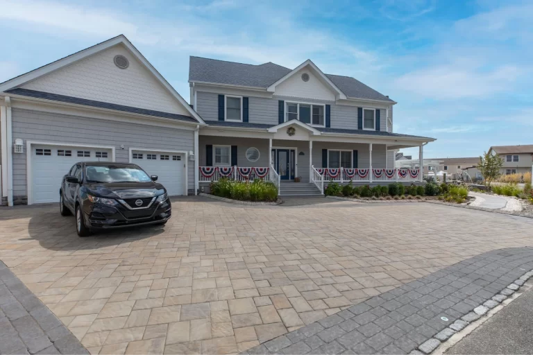 Two-story gray house with a decorated porch, wide driveway, and a black car parked in front.