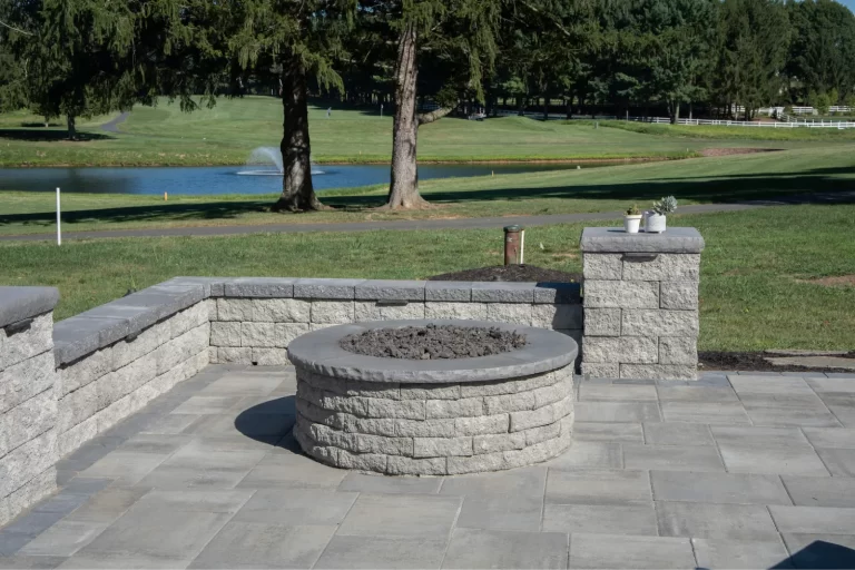 Stone fire pit on a patio with a golf course, pond, and trees in the background.