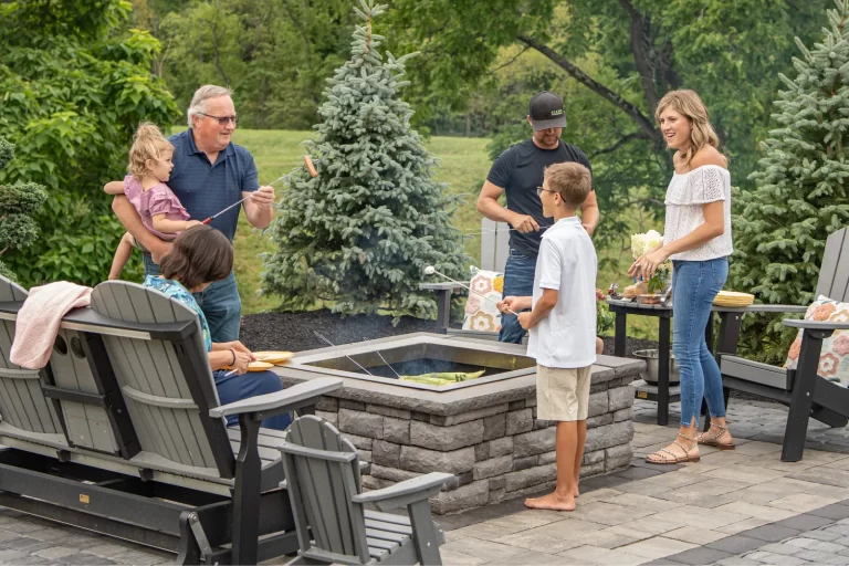 A family gathers around a backyard fire pit, roasting marshmallows and enjoying time together outdoors.