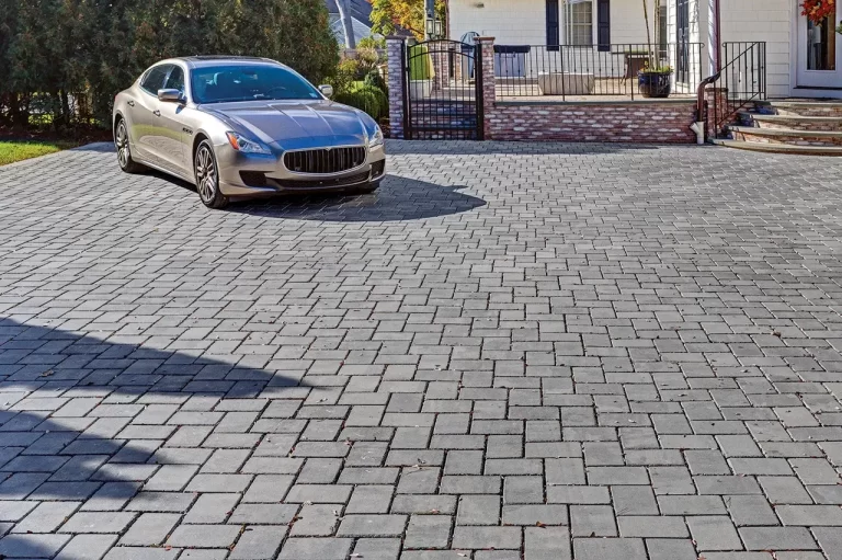 Silver car parked on a spacious driveway with gray stone pavers in front of a house with a brick porch.