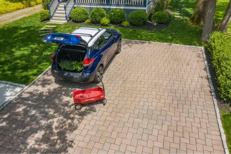 A blue SUV with its trunk open is parked on a brick driveway next to a red wagon.
