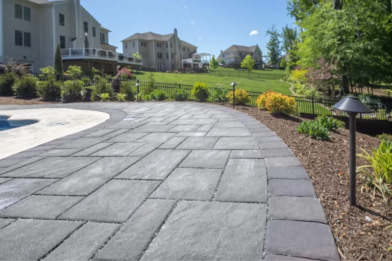 Gray stone patio with landscaped garden and suburban houses in the background on a sunny day.