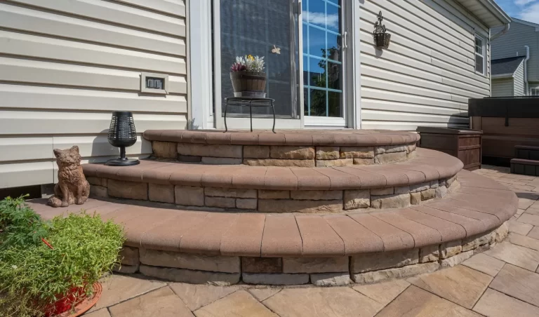 Three curved stone steps lead to a patio door, with potted plants, a cat statue, and outdoor decor.
