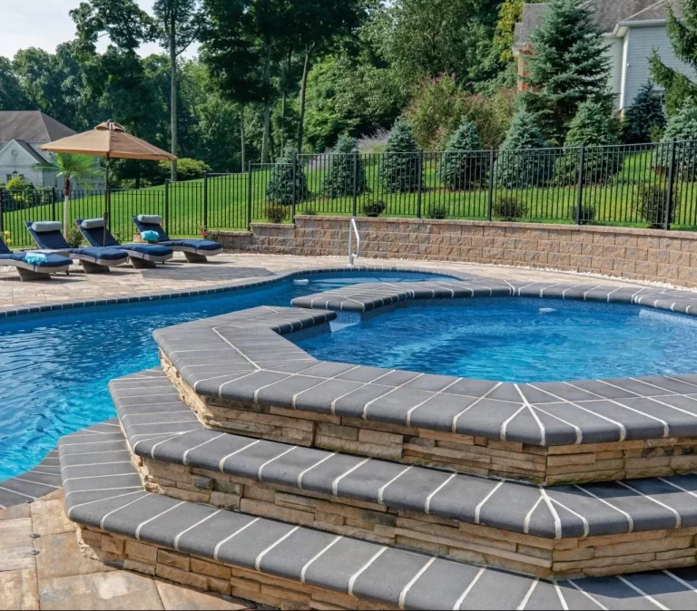 Outdoor swimming pool with a raised circular hot tub, lounge chairs, and trees in the background.