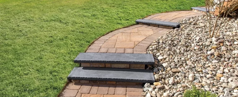 Curved stone walkway with steps, bordered by green grass and a rocky landscape area.
