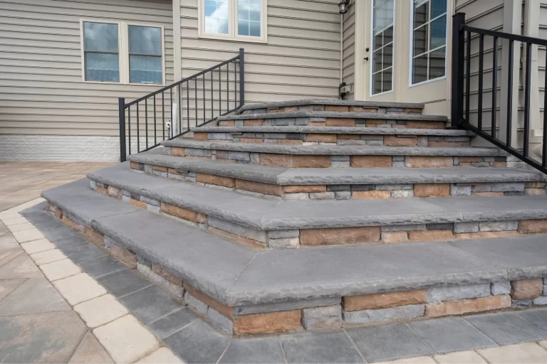 Stone steps with black metal railing lead to a house with beige siding and several windows.
