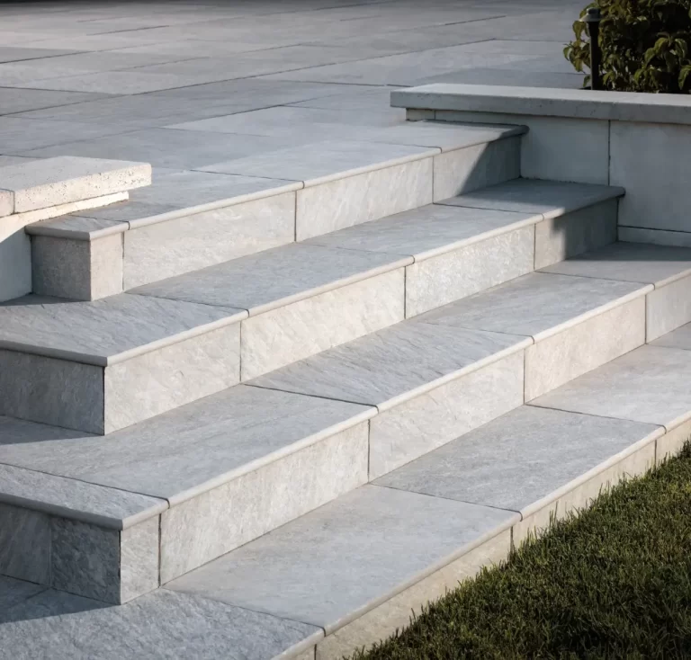 Four wide stone steps lead up to a patio, bordered by grass and a small raised planter.