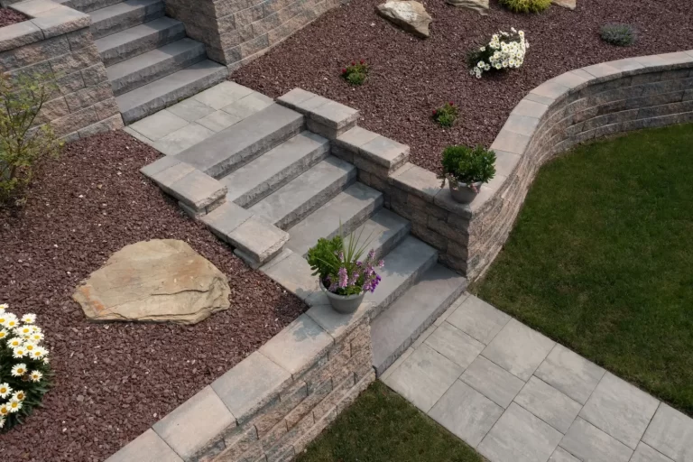 Stone steps and retaining walls with potted plants and flowers, surrounded by mulch and green grass.