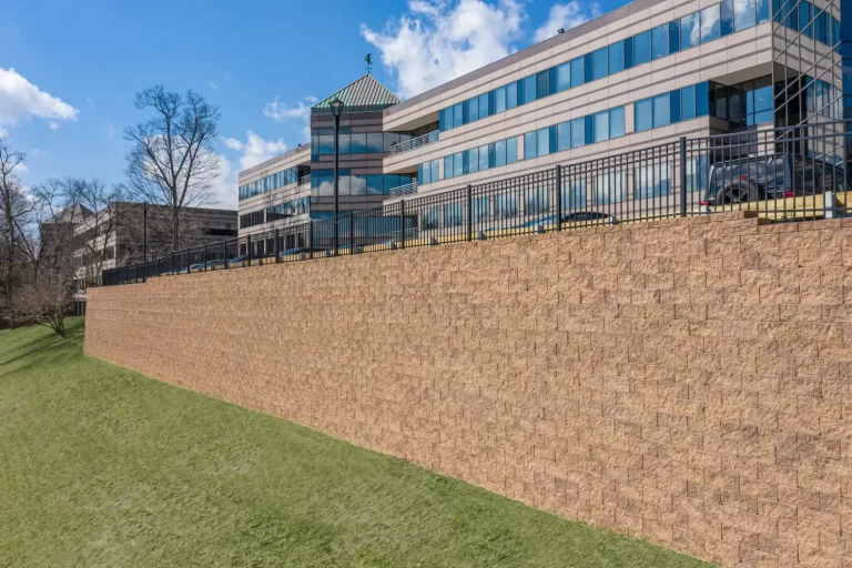 A tall retaining wall supports a grassy slope below a modern office building with glass windows.