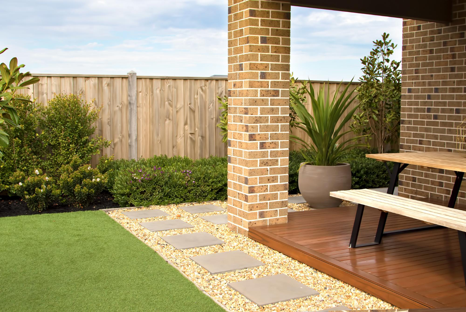 83 (1) Modern backyard with brick patio, wooden table, potted plants, stone path, and artificial grass.