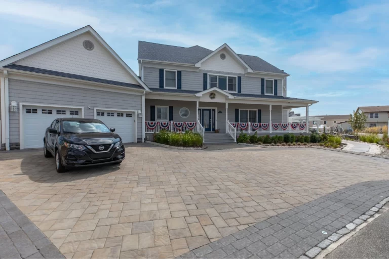 Two-story house with a large driveway, a black car, and patriotic bunting on the front porch railing.